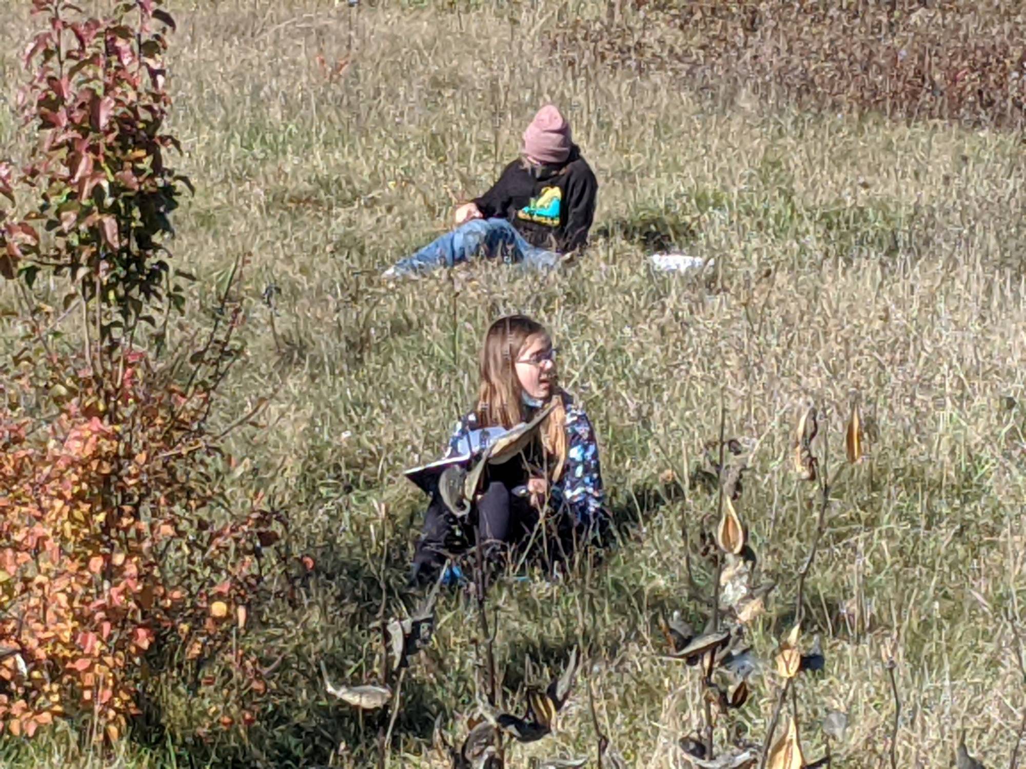 Students writing in notebooks while sitting in tall grass
